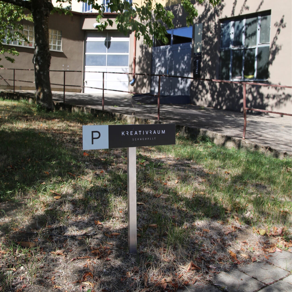 Markierter Parkplatz mit Schild vor dem Eingang der Schwelhalle.