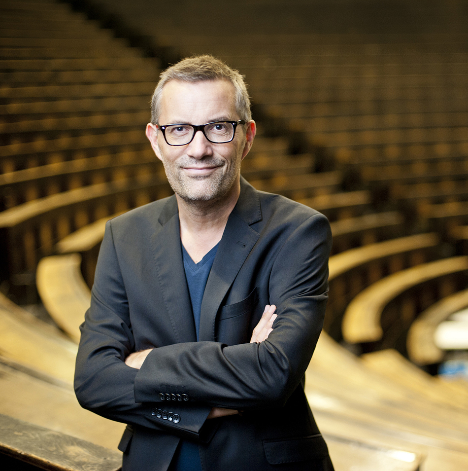 Gerriet Danz mit Sakko steht mit verschränkten Armen in einem leeren Hörsaal